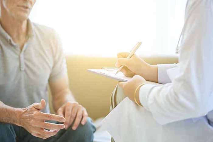 Faceless view of senior man talking to doctor in bright light while taking notes on clipboard